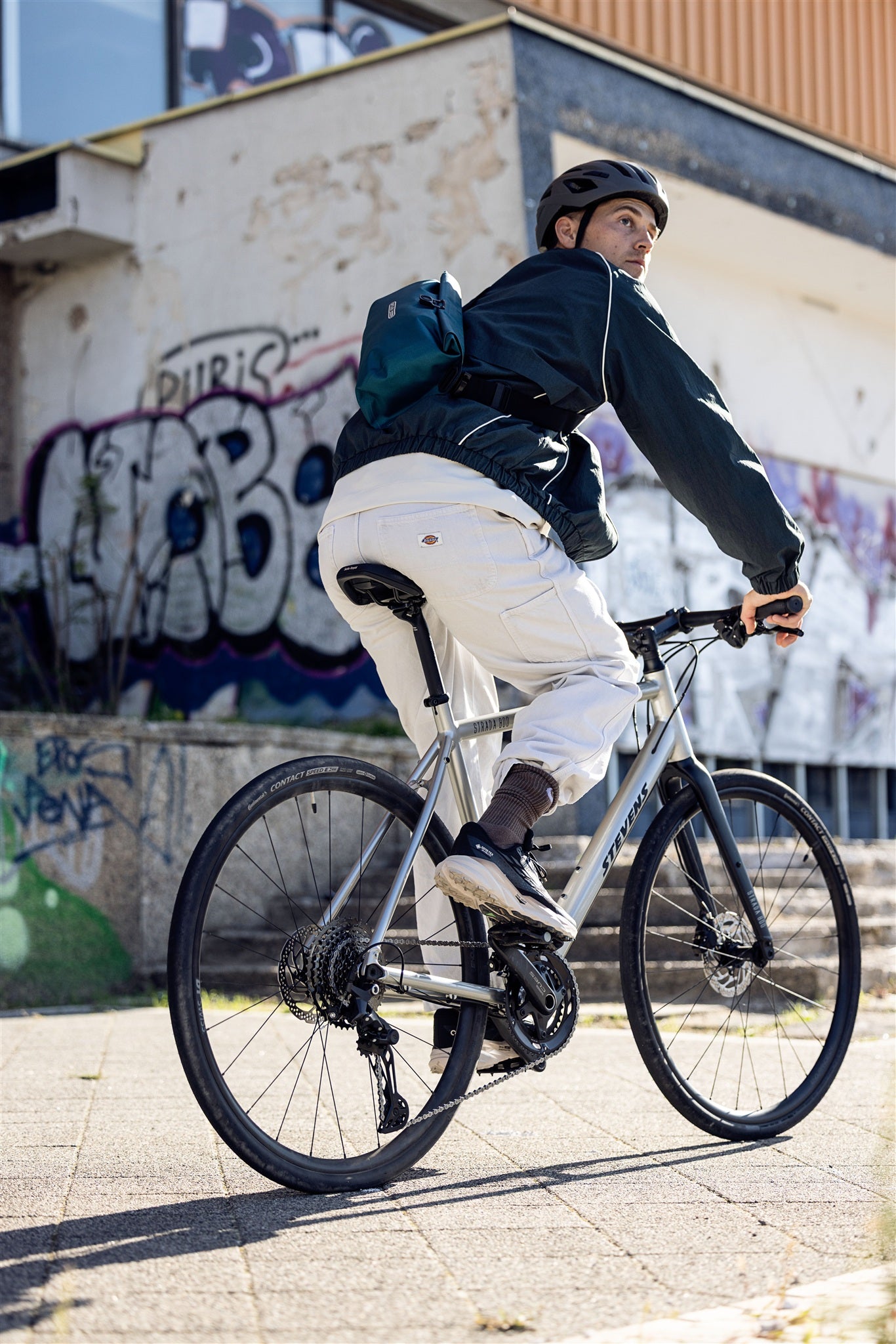 Radfahrer mit petrolfarbener ORTLIEB Velo-Sling Flex Hüfttasche in urbaner Umgebung mit Graffiti.